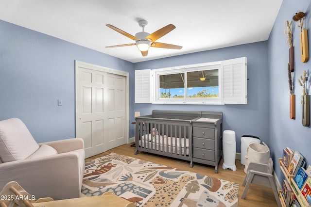 bedroom featuring a ceiling fan, wood finished floors, a closet, a nursery area, and baseboards