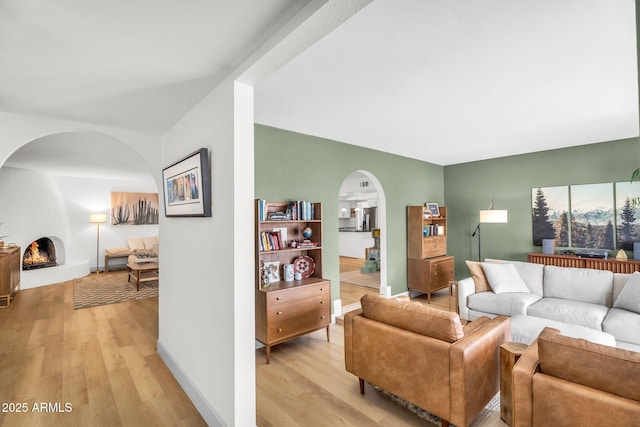 living room featuring a large fireplace, arched walkways, light wood-style floors, and baseboards