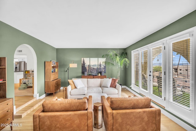 living room with arched walkways, visible vents, light wood-style flooring, and baseboards