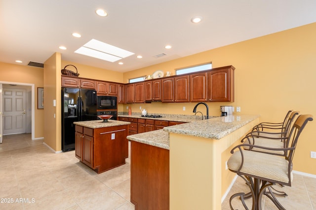 kitchen with black appliances, a kitchen breakfast bar, a center island, a peninsula, and a skylight