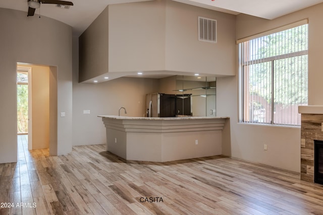 15972 N 115th Way, Scottsdale, AZ 85255 - kitchen featuring light wood-style flooring, ceiling fan, a tiled fireplace, a towering ceiling, and stainless steel fridge