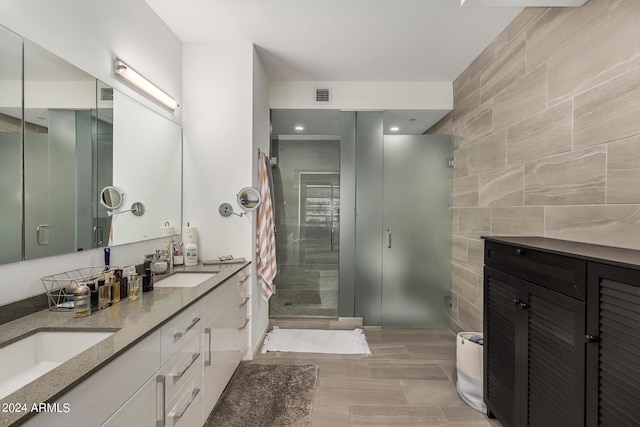 bathroom with double vanity, a stall shower, visible vents, a sink, and tile walls