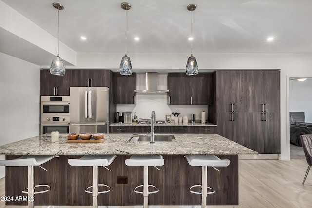 kitchen with wall chimney exhaust hood, dark brown cabinets, a sink, and stainless steel appliances