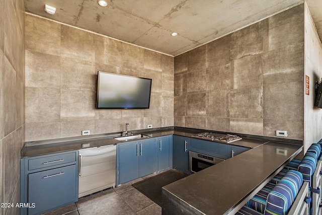 kitchen with dark countertops, dishwashing machine, oven, blue cabinets, and a sink