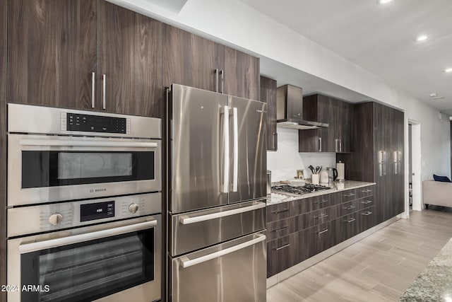 kitchen featuring light stone counters, recessed lighting, appliances with stainless steel finishes, dark brown cabinets, and wall chimney exhaust hood