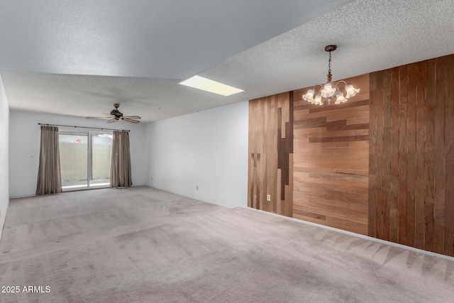 carpeted spare room featuring ceiling fan with notable chandelier, wooden walls, and a textured ceiling