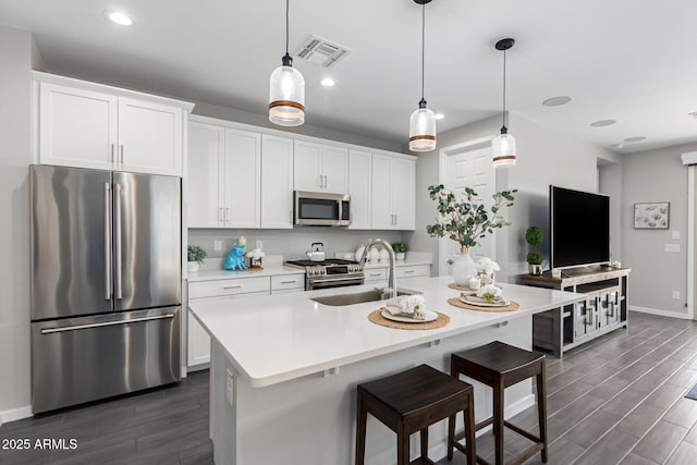 kitchen with white cabinets, sink, premium appliances, and an island with sink