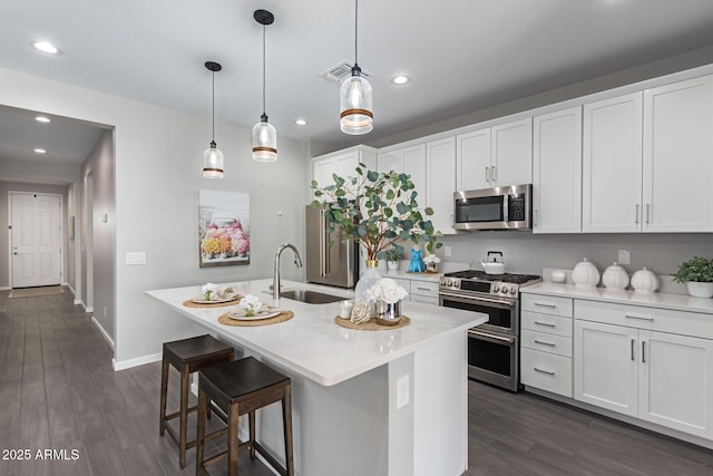 kitchen with decorative light fixtures, white cabinets, appliances with stainless steel finishes, and a kitchen island with sink