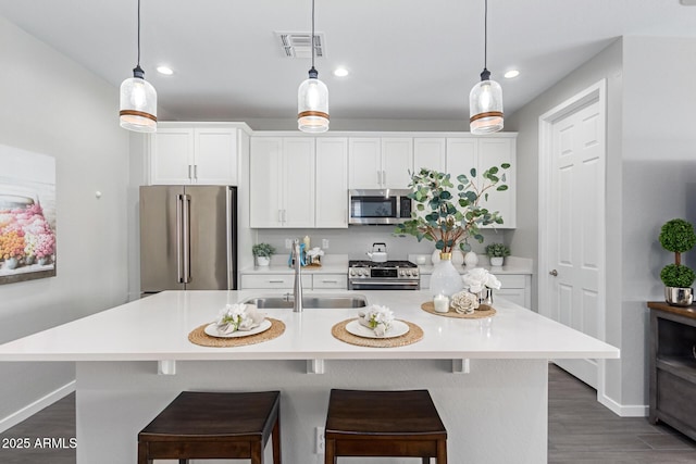 kitchen with hanging light fixtures, an island with sink, sink, and stainless steel appliances