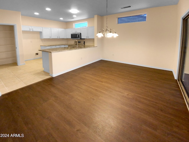 kitchen featuring white cabinetry, light hardwood / wood-style floors, appliances with stainless steel finishes, a notable chandelier, and kitchen peninsula