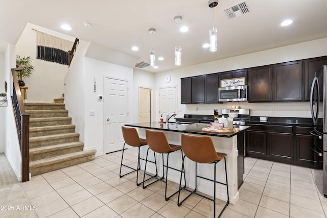 kitchen featuring light tile patterned floors, an island with sink, appliances with stainless steel finishes, pendant lighting, and sink