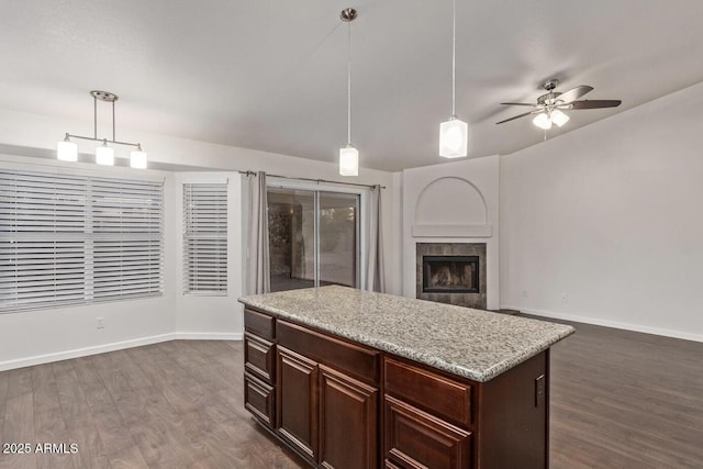 kitchen featuring a kitchen island, decorative light fixtures, dark hardwood / wood-style flooring, a tiled fireplace, and light stone countertops