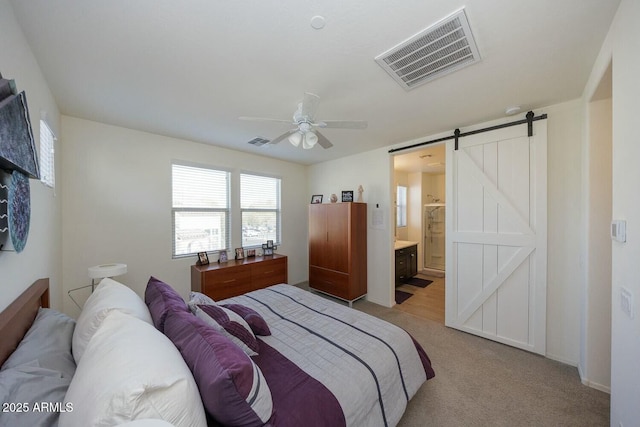 carpeted bedroom with a barn door, connected bathroom, and ceiling fan