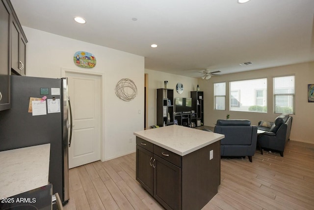 kitchen with dark brown cabinetry, light hardwood / wood-style flooring, stainless steel refrigerator, and a kitchen island