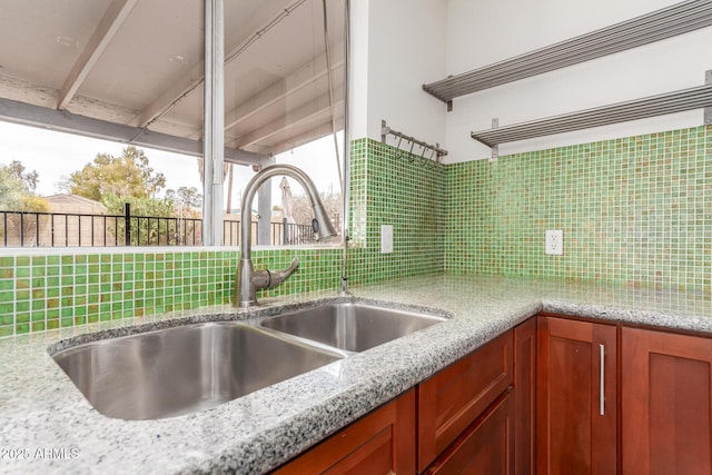 kitchen with brown cabinets, backsplash, a sink, and light stone countertops