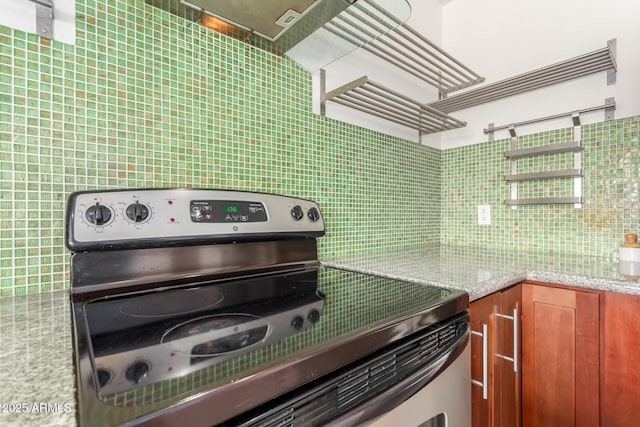 kitchen with light stone counters, brown cabinetry, stainless steel range with electric stovetop, and decorative backsplash