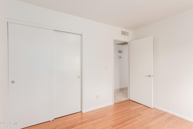 unfurnished bedroom with baseboards, light wood-style flooring, visible vents, and a closet