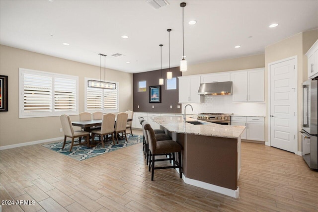 kitchen with a center island with sink, sink, white cabinetry, and pendant lighting