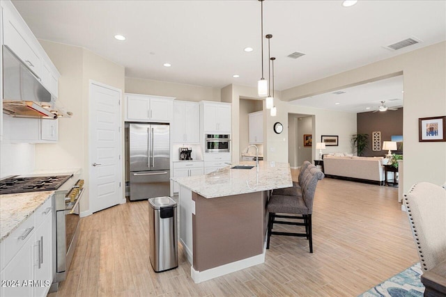 kitchen with a kitchen breakfast bar, an island with sink, stainless steel appliances, and white cabinetry