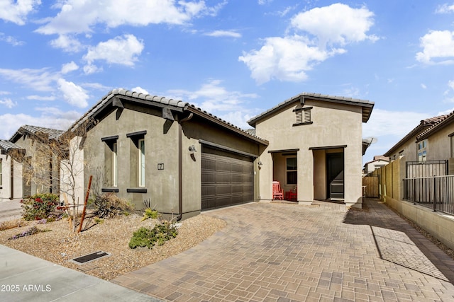 view of front of house with decorative driveway, an attached garage, fence, and stucco siding