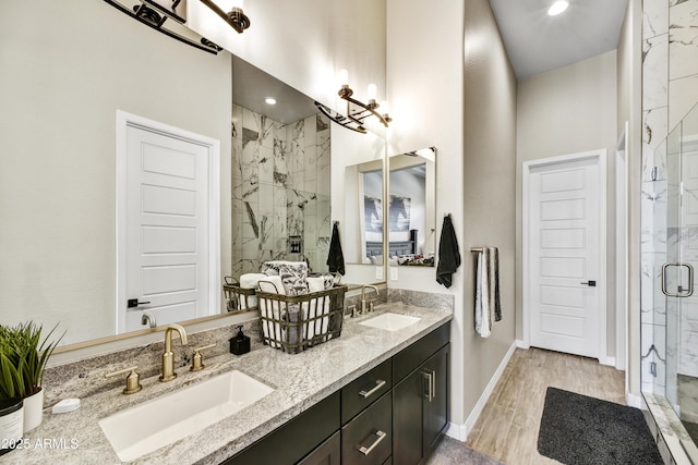 full bathroom featuring wood finished floors, a sink, a marble finish shower, and double vanity