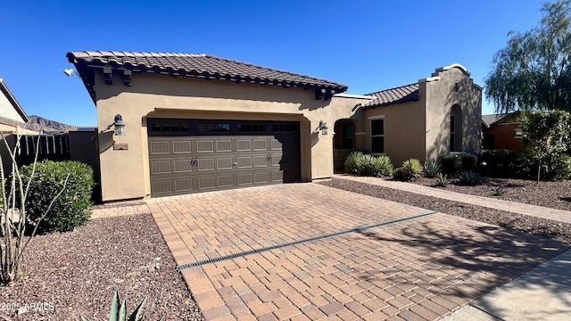 mediterranean / spanish house with decorative driveway, a tiled roof, an attached garage, and stucco siding