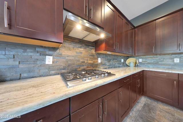 kitchen featuring light stone counters, stainless steel gas cooktop, under cabinet range hood, and decorative backsplash