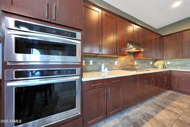 kitchen featuring appliances with stainless steel finishes, light stone counters, under cabinet range hood, backsplash, and recessed lighting