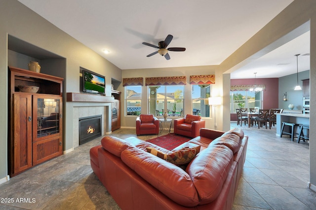 living room featuring a fireplace, baseboards, and ceiling fan with notable chandelier