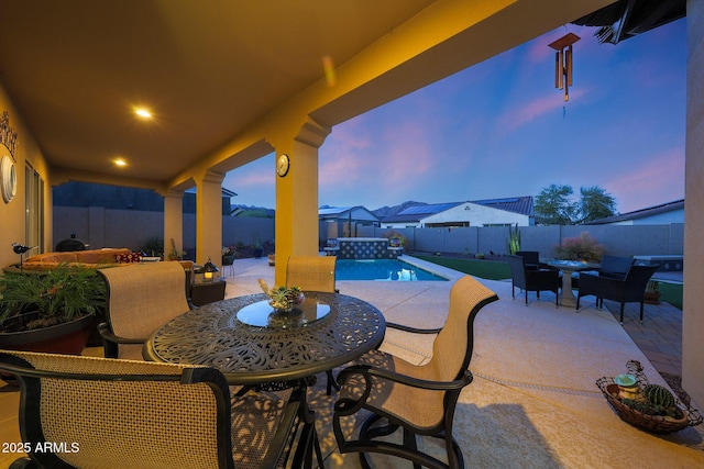 patio terrace at dusk featuring a fenced backyard, a fenced in pool, and outdoor dining space