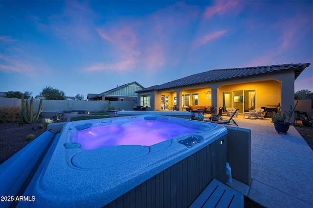 pool at dusk featuring a patio area, fence, a pool, and a hot tub