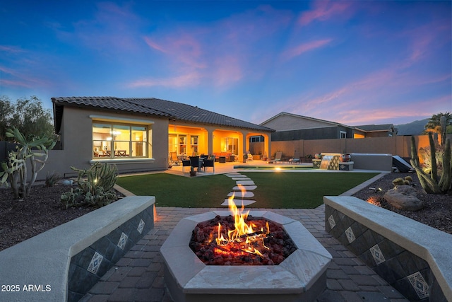 back of house at dusk with an outdoor living space with a fire pit, a yard, stucco siding, a patio area, and a fenced backyard