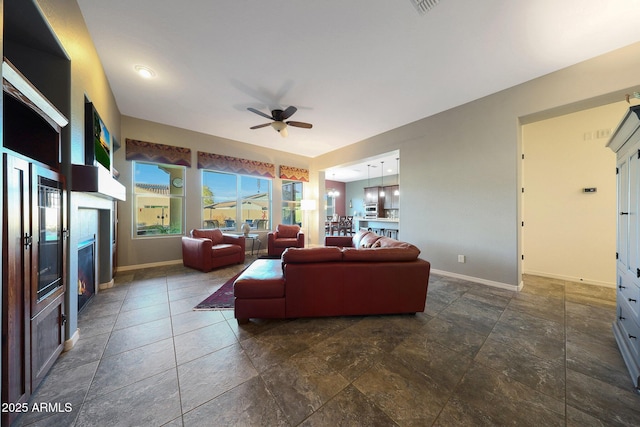 living area featuring a warm lit fireplace, ceiling fan, and baseboards