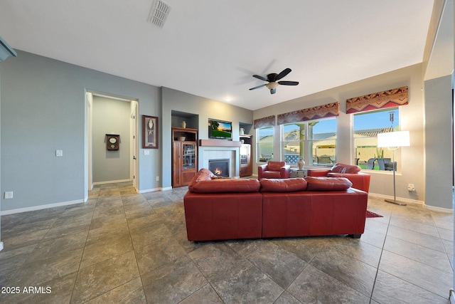 living room with a warm lit fireplace, visible vents, baseboards, built in features, and a ceiling fan