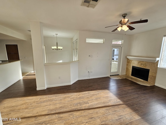 unfurnished living room featuring a fireplace, dark hardwood / wood-style flooring, and ceiling fan with notable chandelier