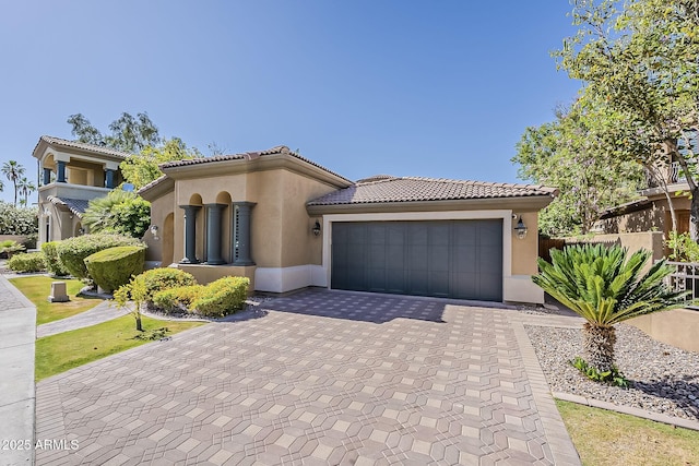 mediterranean / spanish-style home featuring stucco siding, decorative driveway, a garage, a tiled roof, and fence