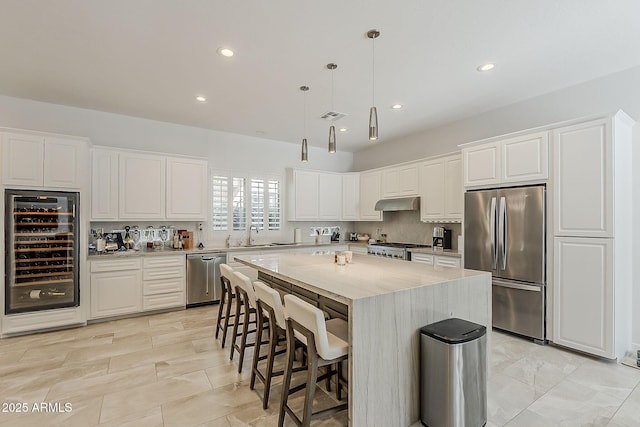 kitchen with appliances with stainless steel finishes, wine cooler, white cabinets, a breakfast bar area, and recessed lighting