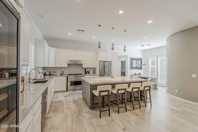 kitchen with appliances with stainless steel finishes, a sink, under cabinet range hood, white cabinets, and a large island