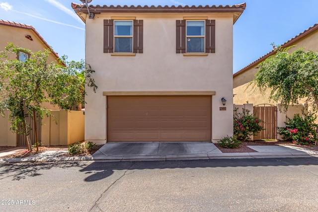 mediterranean / spanish home featuring an attached garage, driveway, stucco siding, and a gate
