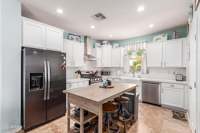 kitchen with wall chimney range hood, light countertops, appliances with stainless steel finishes, and visible vents