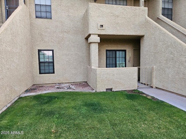 view of exterior entry featuring stucco siding and a lawn