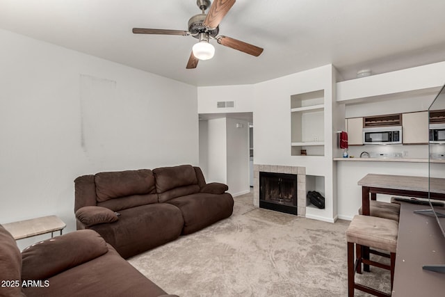 living room featuring light colored carpet, a tile fireplace, and ceiling fan