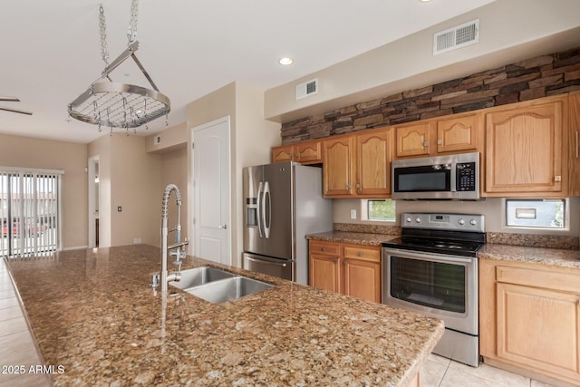 kitchen featuring appliances with stainless steel finishes, a sink, stone counters, light tile patterned flooring, and an island with sink