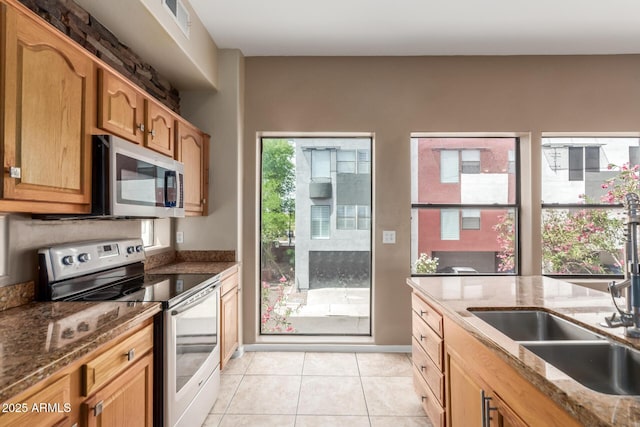 kitchen with appliances with stainless steel finishes, a sink, dark stone counters, and light tile patterned floors