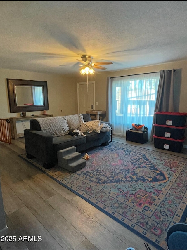 living room with ceiling fan, a textured ceiling, and wood-type flooring