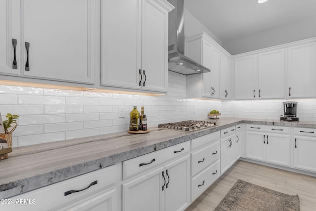 kitchen featuring light stone countertops, stainless steel gas stovetop, white cabinetry, wall chimney range hood, and tasteful backsplash