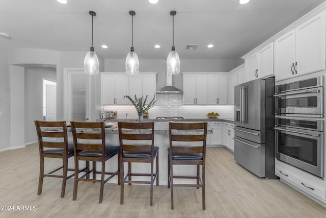 kitchen with appliances with stainless steel finishes, hanging light fixtures, white cabinets, and wall chimney exhaust hood