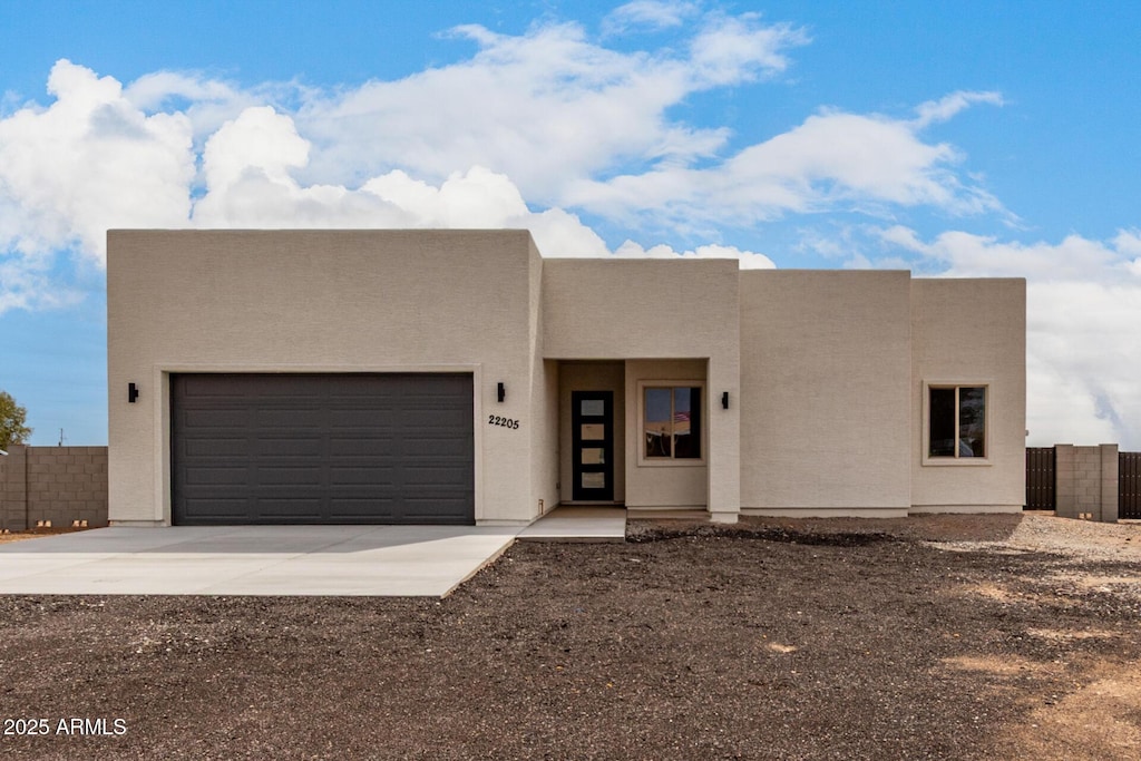 adobe home with concrete driveway, stucco siding, fence, and an attached garage
