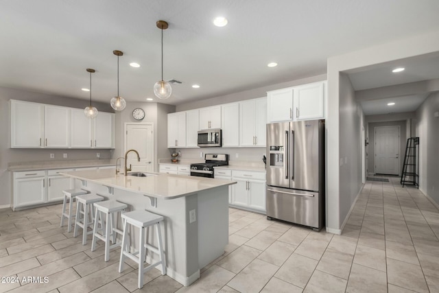 kitchen with a center island with sink, white cabinets, pendant lighting, and appliances with stainless steel finishes