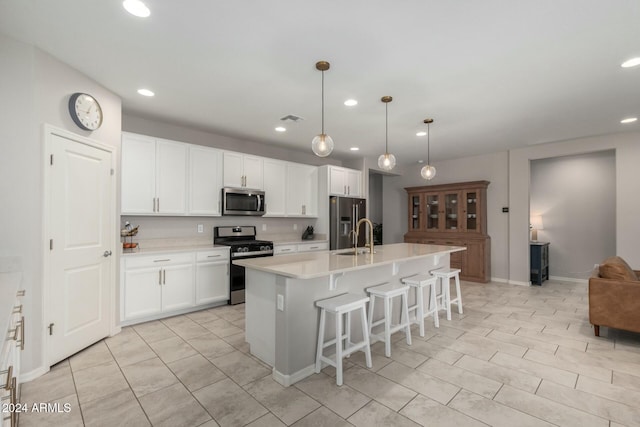 kitchen with a center island with sink, decorative light fixtures, white cabinets, and appliances with stainless steel finishes